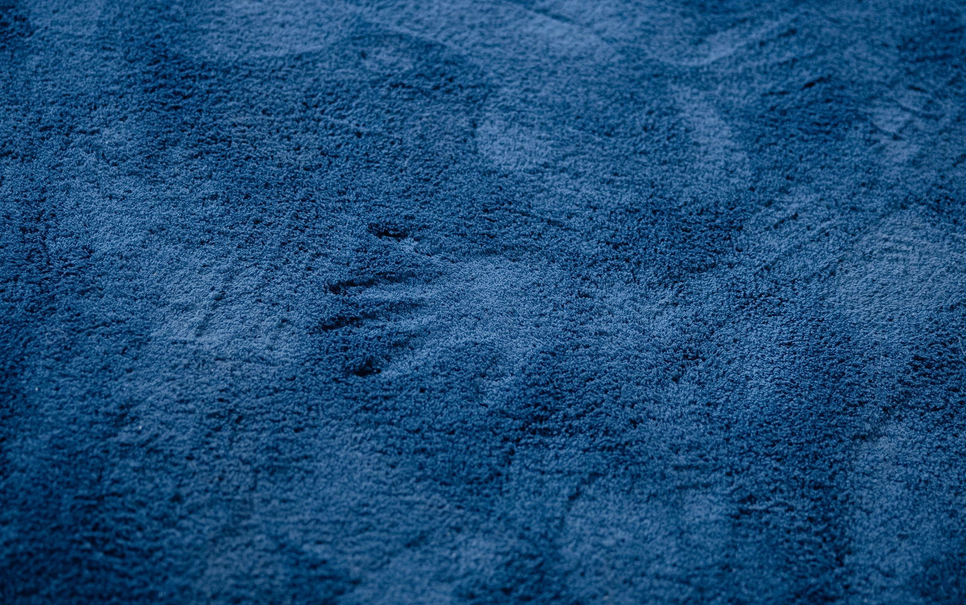 Fotografia dywanu znajdującego się na sali wystawowej galerii sztuki, jest granatowy i miękki, na środku ślad po odbitej dłoni